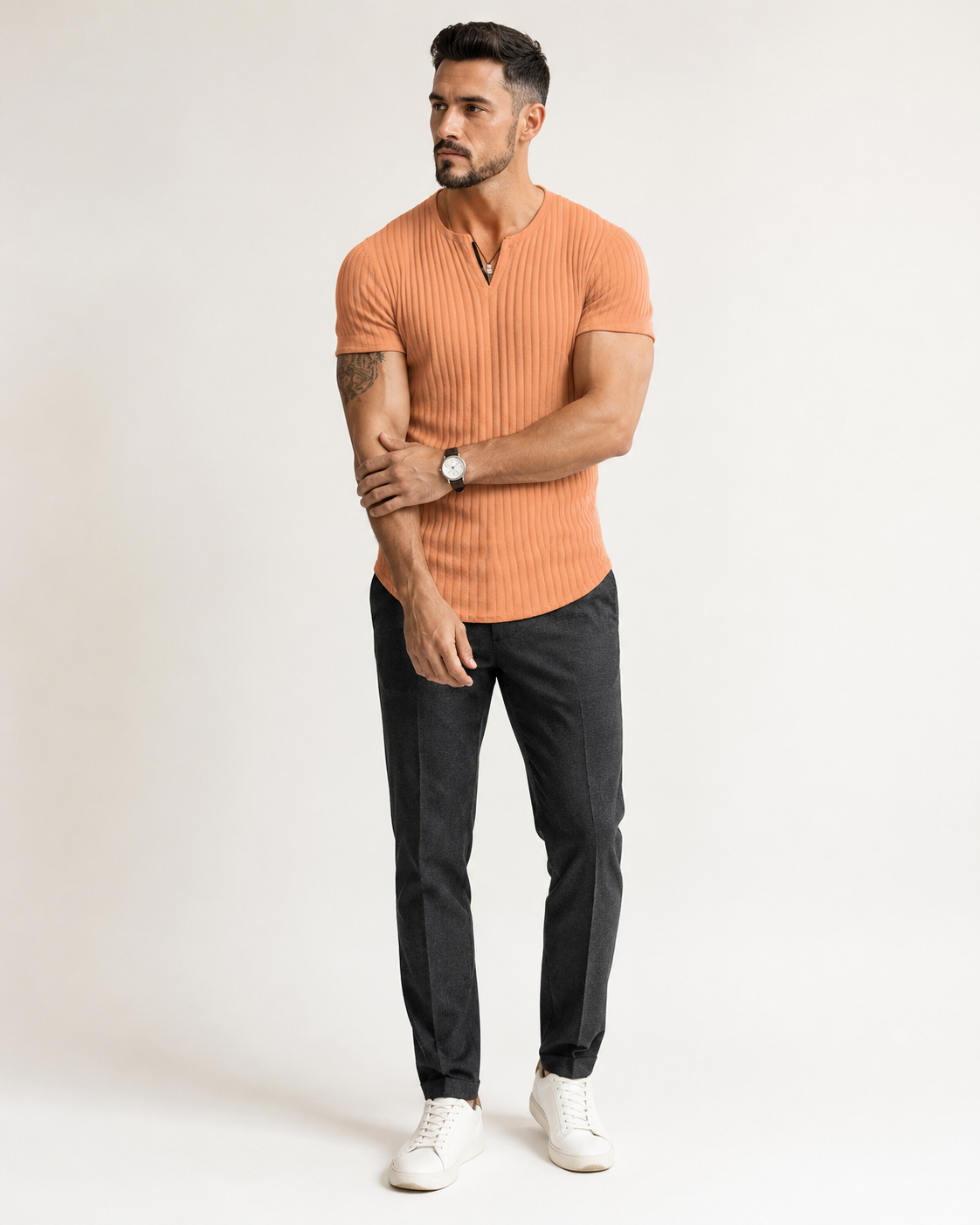 Aikuinen miesmalli oranssissa ribbineulotussa slim fit Henley-paidassa luonnonvalkoisessa studiossa